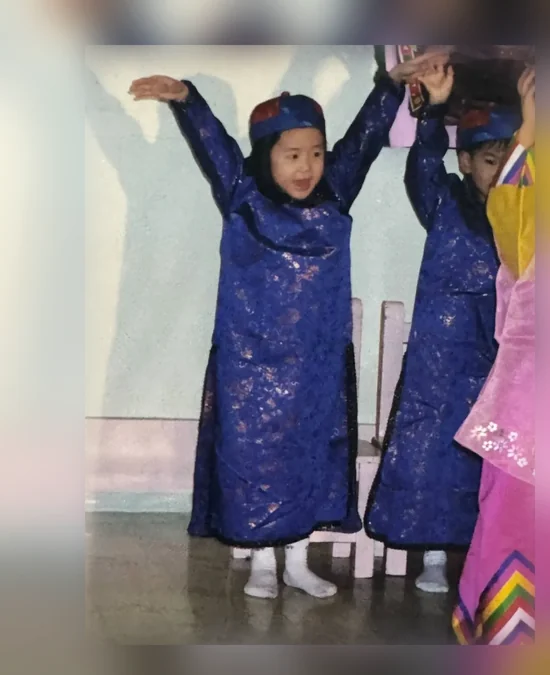 Julie as a child on stage in a blue costume, arms raised, Edmonton